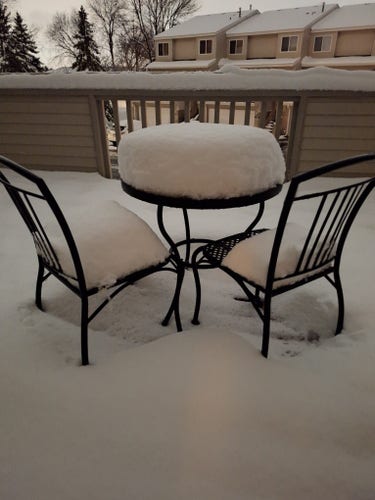 A Bistro table on a snow-covered deck supports a cushion of about 10 inches of snow.