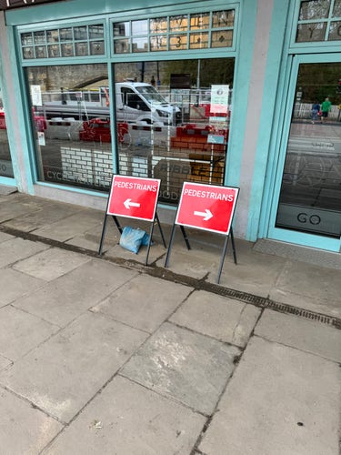 Two temporary signs outside a closed shop. One tells pedestrians to go left and the other one tells pedestrians to go right