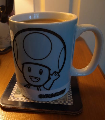 Small blue mug on a bedside cabinet, it has a character, smiling and waving, and wearing a mushroom like hat, 