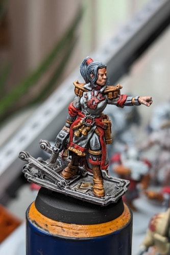 A mostly painted Warhammer 40k miniature (sort of, not an official model) a female captain standing on an open door holding a laspistol with a red handprint on her white tunic.
