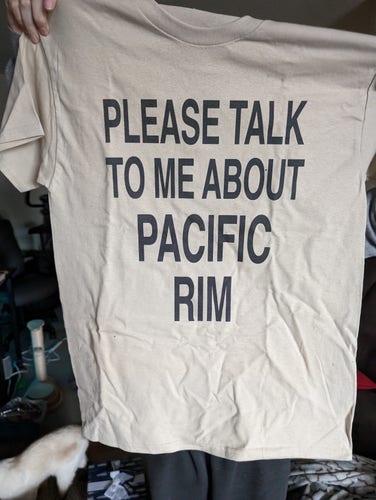 Cream-white colored t-shirt with the text "Please talk to me about Pacific Rim"