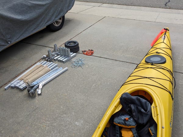 Looking down at my driveway. On the right is my yellow kayak. On the left are the disassembled parts of my kayak cart. It's a mix of standard aluminum extrusion parts bolted or welded together along with wheels, bungee cords, and large latching cotter pins.