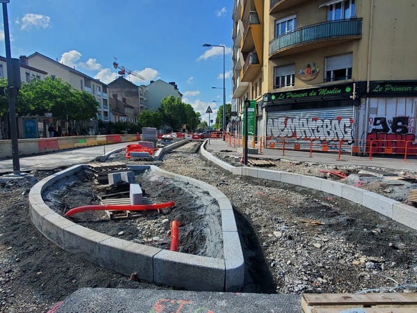 La route de Vienne en chantier au carrefour de la rue Challemel Lacour. Les bordures sont posées, mais c'est encore en gravier. On devine le futur quai de l'arrêt de bus.
Les piétons peuvent longer le chantier.