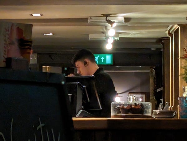 A photo of a member of bar staff serving a customer while wearing a large black earpiece.