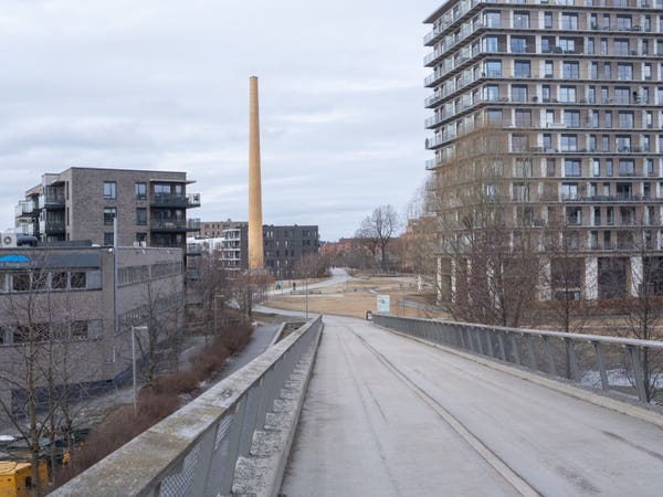 From a pedestrian road towards town. Apartment buildings on both sides. An old factory chimney ahead.