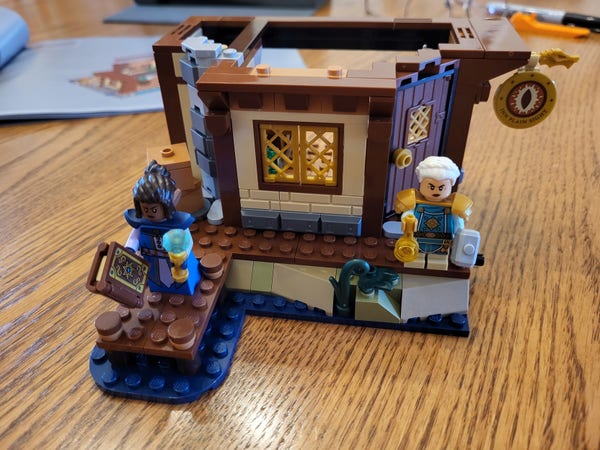 Bag 2 of the Lego Dungeons & Dragons set, completed. The inn has a sign now, and some half-timbered framing at the top of the first floor. There's also a chimney around the side with some boxes of supplies in front. A wizard in blue and purple has joined the cleric from the previous step.