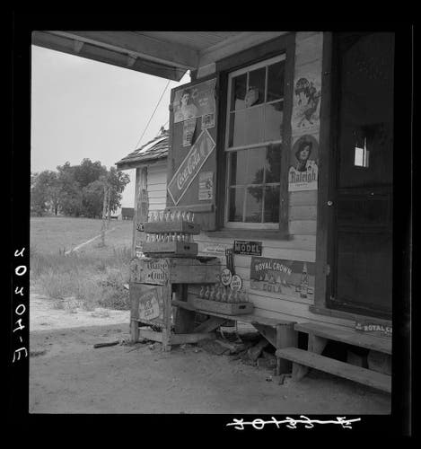  The image depicts a rustic scene of an old-fashioned filling station. The structure appears weathered, with peeling paint and signs attached to its exterior walls, suggesting a long history of use and exposure to the elements. The signage includes advertisements for cigarettes and other products, indicating that this location was once a hub of local commerce.

The filling station is situated in what looks like a rural area with a dirt road leading up to it. Surrounding structures are not visible, giving an impression of isolation. The overall condition of the building hints at a certain level of disrepair or abandonment, yet the signs remain, as if waiting for the return of activity.

Inside the filling station, there's a collection of old items and signage that add to the vintage feel of the place. These could be remnants from when the station was in operation, perhaps serving both as decorative pieces and functional items. The absence of people in the image conveys a sense of stillness, as if captured during a quiet moment away from hustle and bustle.

The image itself is described as vintage, which could imply that it was taken some time ago, capturing a slice of history and local culture. The text at the bottom suggests that this filling station might be located in Granville County, North Carolina, adding geographical context to the scene.

Overall, the image evokes nostalgia for times when such establishments were  [...]