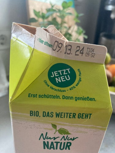 A picture of a milk carton with the old design without plastic lid. Printed in green „Now new: without lid - 40% less plastic“