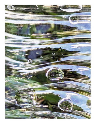 abstract, color. the midday sky and nearby trees are reflecting on each 5 bands between the ridges on the heel of a plastic water bottle. several bubbles of different shapes and sizes magnify the grass under the bottle and/or reflect the sky and trees.