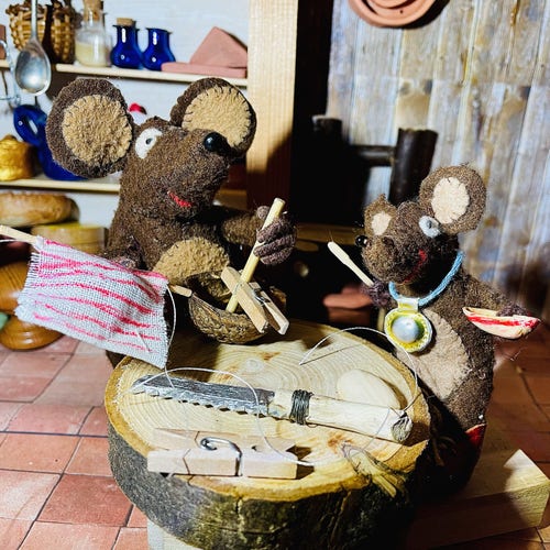 Photo of Minimus and Silvius, the Latin mice, building boats on the kitchen table. Minimus is gluing the mast into a walnut shell. There is a stripy sail on the table, as well as a saw and a spare peg. Silvius is holding a dinghy made from a pistachio shell, and a tiny whittled oar. 
