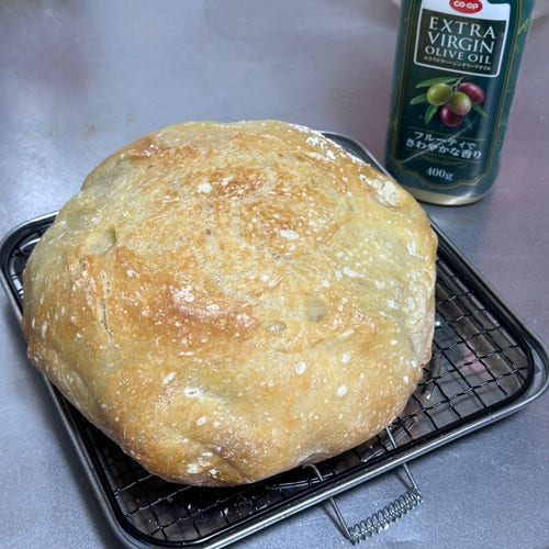 A freshly baked loaf of bread on a cooling rack beside a bottle of extra virgin olive oil.