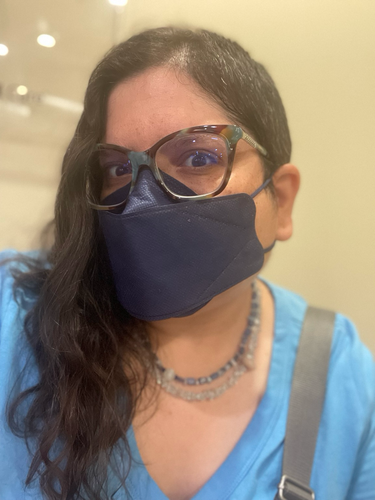 Photo of nonbinary half Indian person with half short, half long, dark brown hair. They are wearing glasses and a navy blue kn95 mask, and a light blue T-shirt.