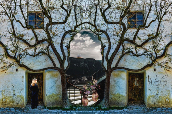 A symmetrical composition presents a mirrored image of a gnarled tree growing out of an old, weathered building with a woman in a full length black dress standing to the left. Through the center, where the tree forks, is a view of a distant hill, with a spiral staircase, topped with an orange car under a cloudy sky.