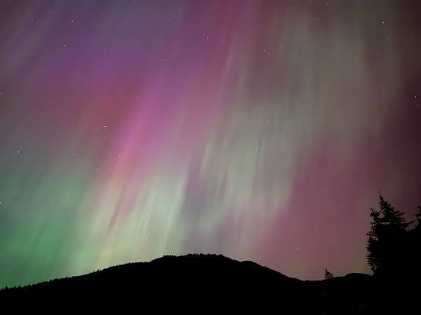 The aurora above a silhouette of a hillside. Pinks and greens dominate