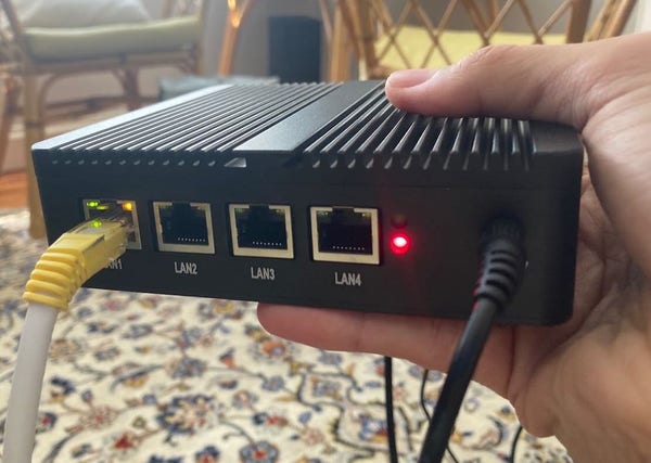 Holding a mini PC and network appliance from AliExpress showing its 4 ethernet ports