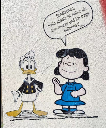 Streetart. A funny comic paste-up with Lucy (Peanuts) and Donald Duck was stuck on a beige exterior wall. Lucy is a little girl with black hair wearing a short blue dress and white shoes. She says while looking at her fingernails: Speech bubble (in German): "Honey, my heels are higher than your level and I'm wearing flats!". Donald Duck, the duck, simply stands next to her with his hand outstretched.