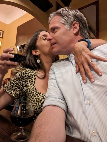 Two people kissing, glass of orange wine in hand.