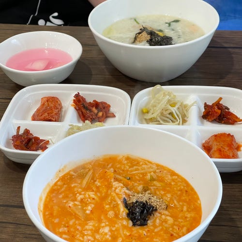 Dwie miski koreańskich dań, jedna z dodatkami z wodorostów, druga z pikantnym pomarańczowym kimchi, w towarzystwie różnych małych dodatków, w tym kimchi i marynowanych warzyw.