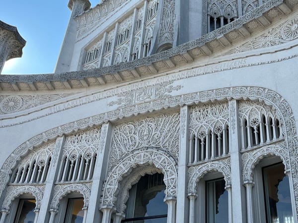 Ornate building facade with intricate stone carvings and arched windows, featuring an inscription that reads "The Earth Is But One Country And Mankind Its Citizens."