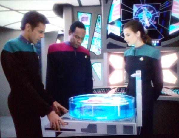 crew members gathered around a digital hologram display running a test on a laboratory table, screens with colored diagrams behind them, very futuristic 