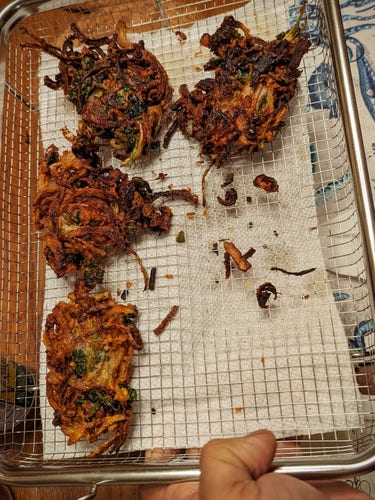 Pakora with sliced onions, green chilli, cilantro leaves in besan, fried brown and crisp and on a metal mesh tray