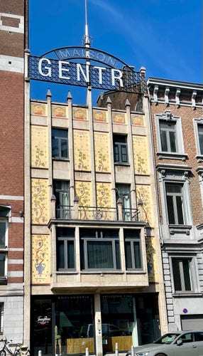 Facade of an art nouveau build. Light yellow with vine tendrils painted on it.