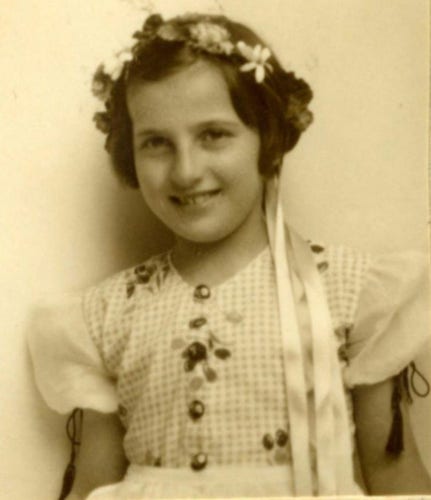 A sepia photo of a girl dressed in folklore dress with short sleeves and floral patterns. She is smiling. She has a garland in her hair.
