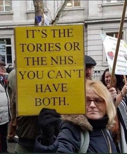 Woman at a protest march holds up a yellow sign that reads: It's the Tories or the NHS. You can't have both.