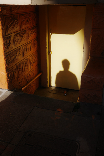 A shadow of a person on a door with light reflecting onto the ground and wall