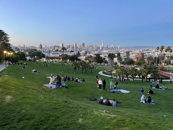 View from the top corner of Dolores Park towards downtown, shot at dusk. The park is still quite crowded, and the last rays of the sun are reflecting off the skyscrapers.