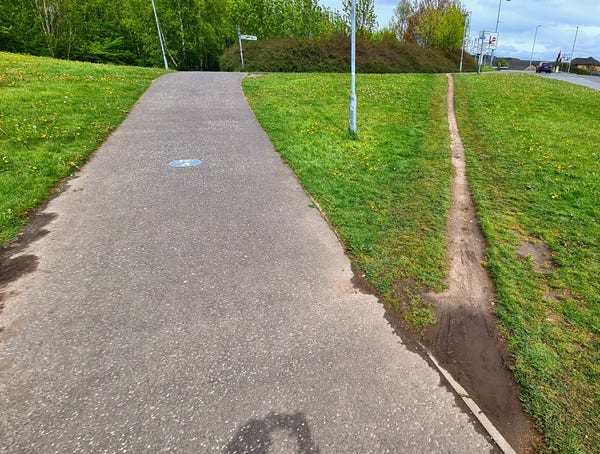 Two alternatovr paths up a small slope. The official, indirect paved on on the left, and the shorter unofficial more direct one created by people on the right.