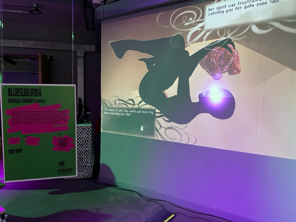 A photo of bluesuburbia at amaze. the sign describing the game is hanging in front of a giant projection of it.