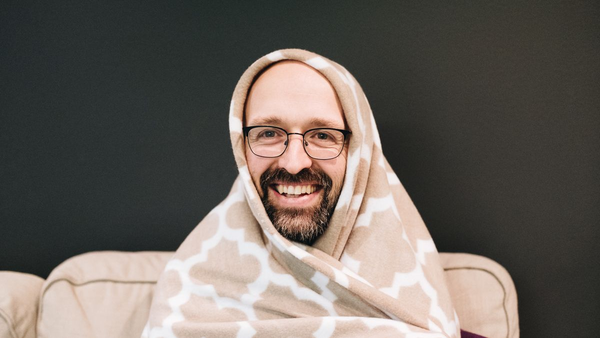 Bearded man wrapped with a blanket over his head, looking overly cheerful.