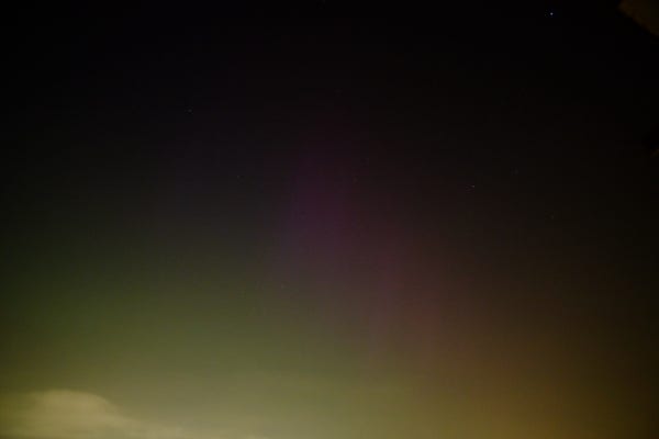A photo of the night sky with a faint purple aurora in he middle. a small cloud is visible bottom right. 
