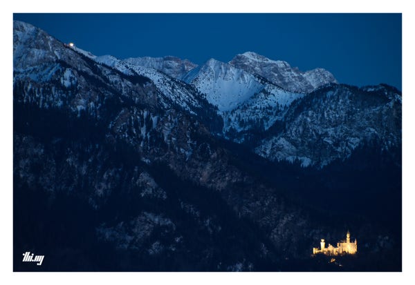 Nighttime view of the brightly illuminated Castle Neuschwanstein in front of snowcovered Tegelberg and Hochplatte in the background, during the last bit of blue hour (13 seconds exposure time)