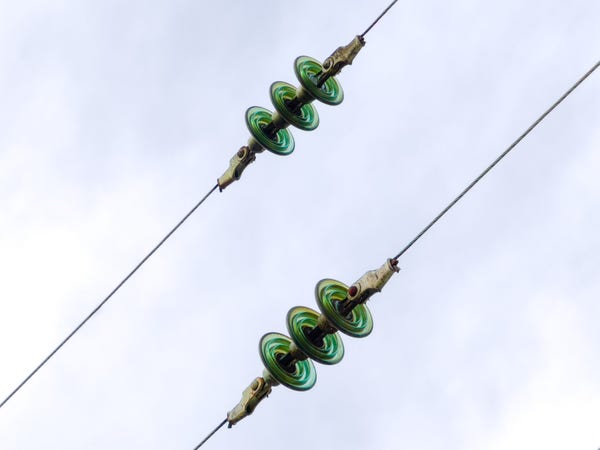 Two wires suspended in the air photographed against the sky. The wires both have a strange thing in the middle, each of which has three green disk things inside of it. 