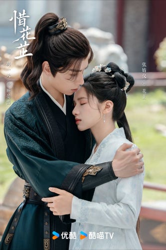 Hu Yitian and Zhang Jingyi embrace. He is on the left in a dark green costume and she is in a pale blue costume. She is leaning her head on his shoulder.