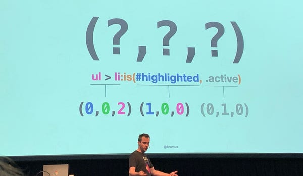 Photo of me at CSS Day 2022, talking about specificity. On the big screen is a bunch of question marks, which seemed fitting for this article.