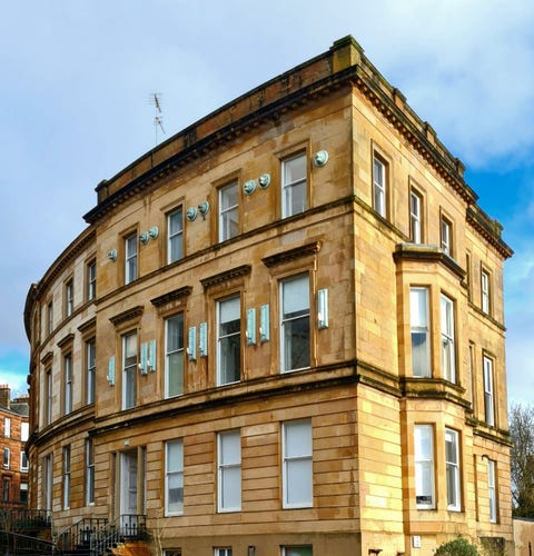 A three storey blonde sandstone tenement with a curved main facade matching the curve of the road on which it is built.