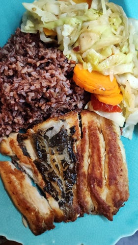 A plate of red rice, sautéed cabbage and carrots, and pan-fried smoked milkfish