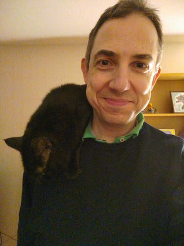 Me smiling standing indoors with a small black fluffy cat on my shoulder
