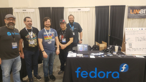Four Fedora contributors next to their Fedora booth at SCaLE 21x, with a ThinkPad that has 3D Pinball Space Cadet running, lol.