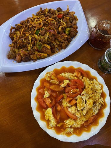 A huge plate of Chinese Spicy Chicken cooked and served with generous amounts of chilli, pepper, and hand pulled noodles, and a plate of Tomato Fried Egg with lots of fresh tomatoes and its juice eaten together with its “scrambled” egg. To the side are containers of condiments including Chilli Oil and Chives.