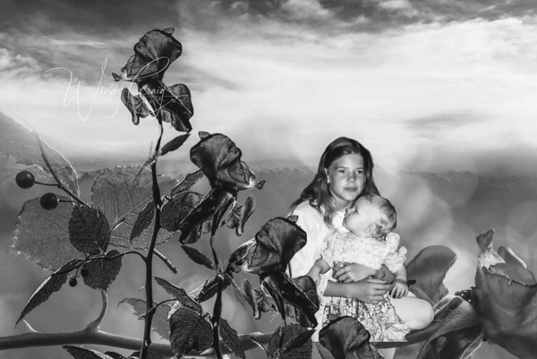 This is a photo collage of a young girl holding a baby girl next to wilted roses. The background is misty mountains.