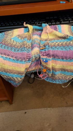 A baby cardigan sweater made of variegated yarn in shades of yellow, beige, blue, purple and pink.