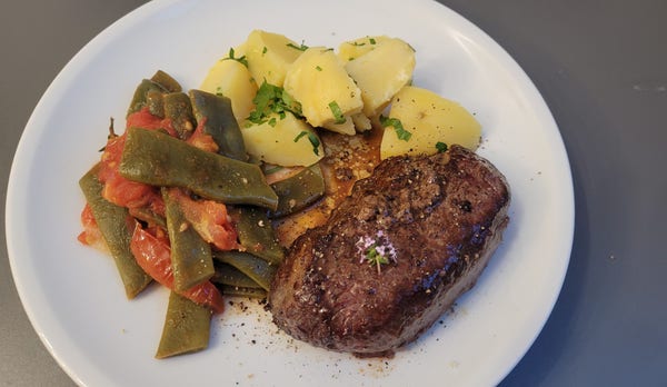 Farbfoto: Auf einem weißen Teller liegen ein Steak, daneben je eine Portion Petersilienkartoffeln und Bohnen-Tomaten-Gemüse. 