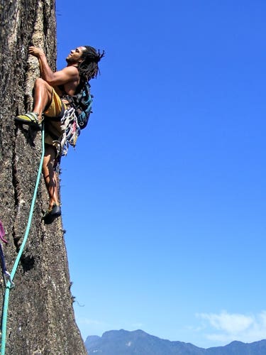 A rock climber focused on lead climbing the beautiful first pitch or Urbanoide route in Rio. The day is sunny and a blue sky can be seen in the background.