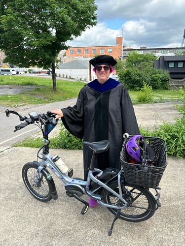 Person wearing academic robes and standing next to a bike