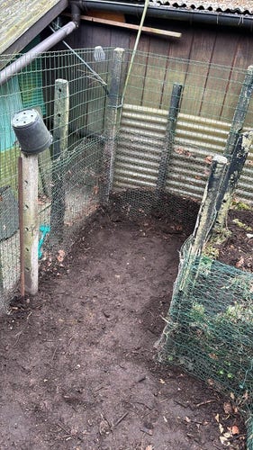 A corner of a yard with corrugated metal and wire fencing, a muddy ground, and no visible animals or people.