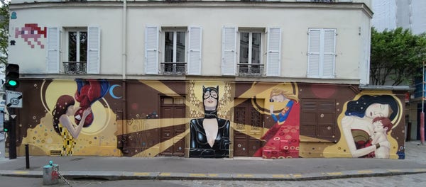 Peinture murale de pleine rue sur toute la façade de rez de chaussée d'un immeuble. On voit le fameux bisou de Spider man, une catwoman, et d'autres personnages.